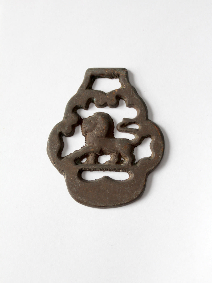 A brass horse harness ornament featuring a lion and a hanging loop, photographed on a clean white background.