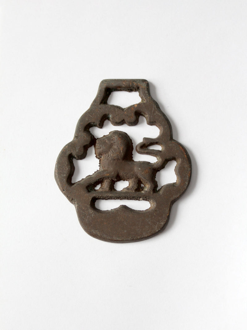 A brass horse harness ornament featuring a lion and a hanging loop, photographed on a clean white background.