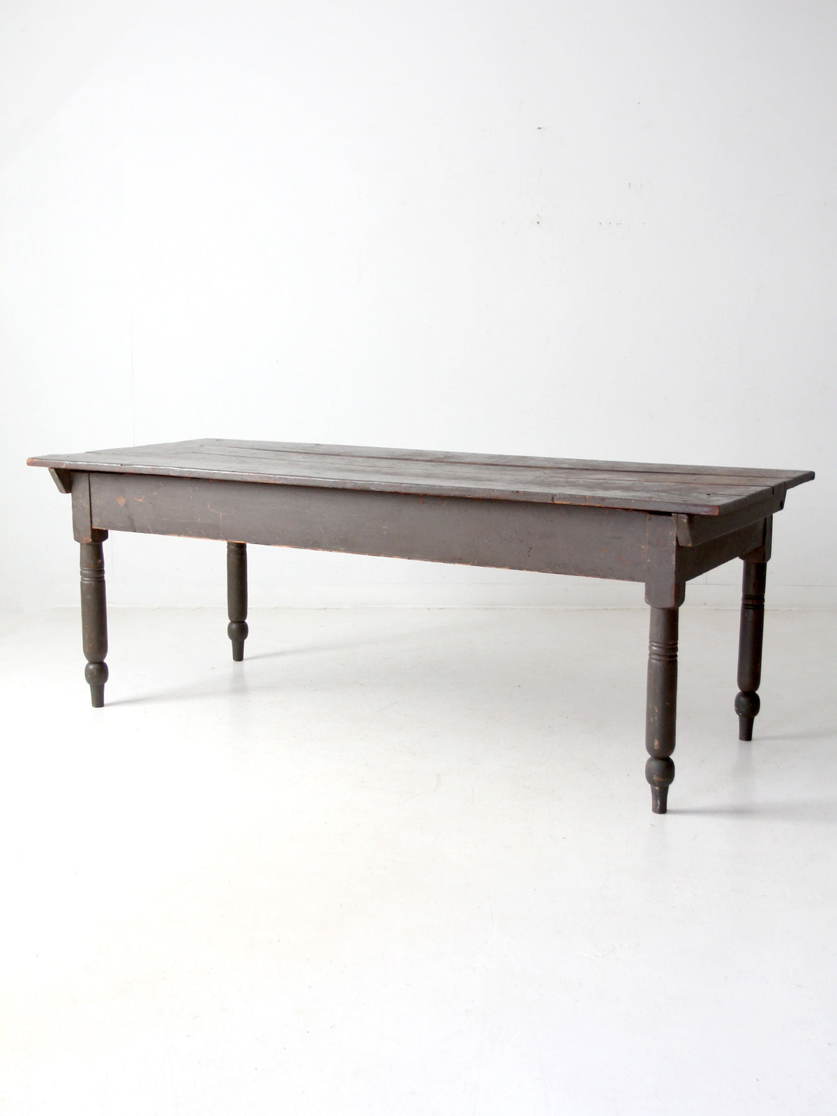 An antique dark brown wooden table with turned legs, photographed against a plain white studio background.