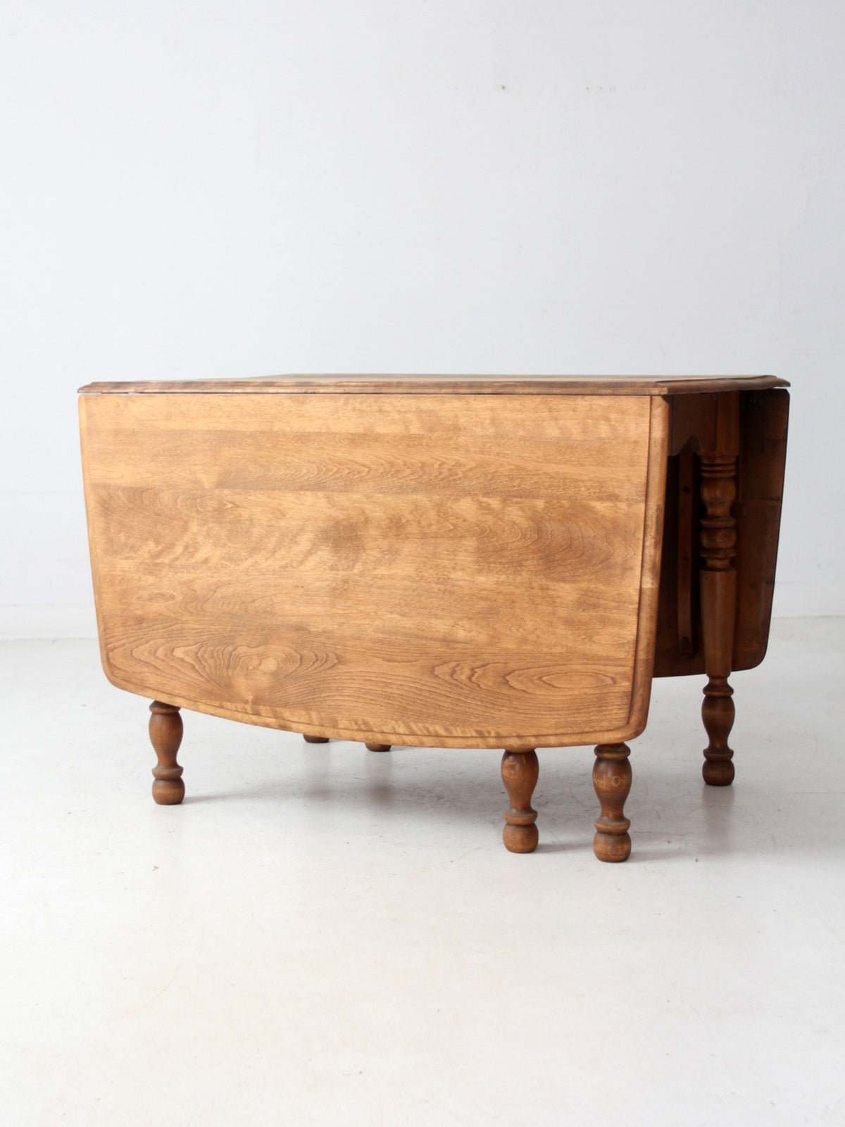 An antique wooden drop-leaf table with a warm medium-brown finish and turned legs, photographed against a plain white studio background.