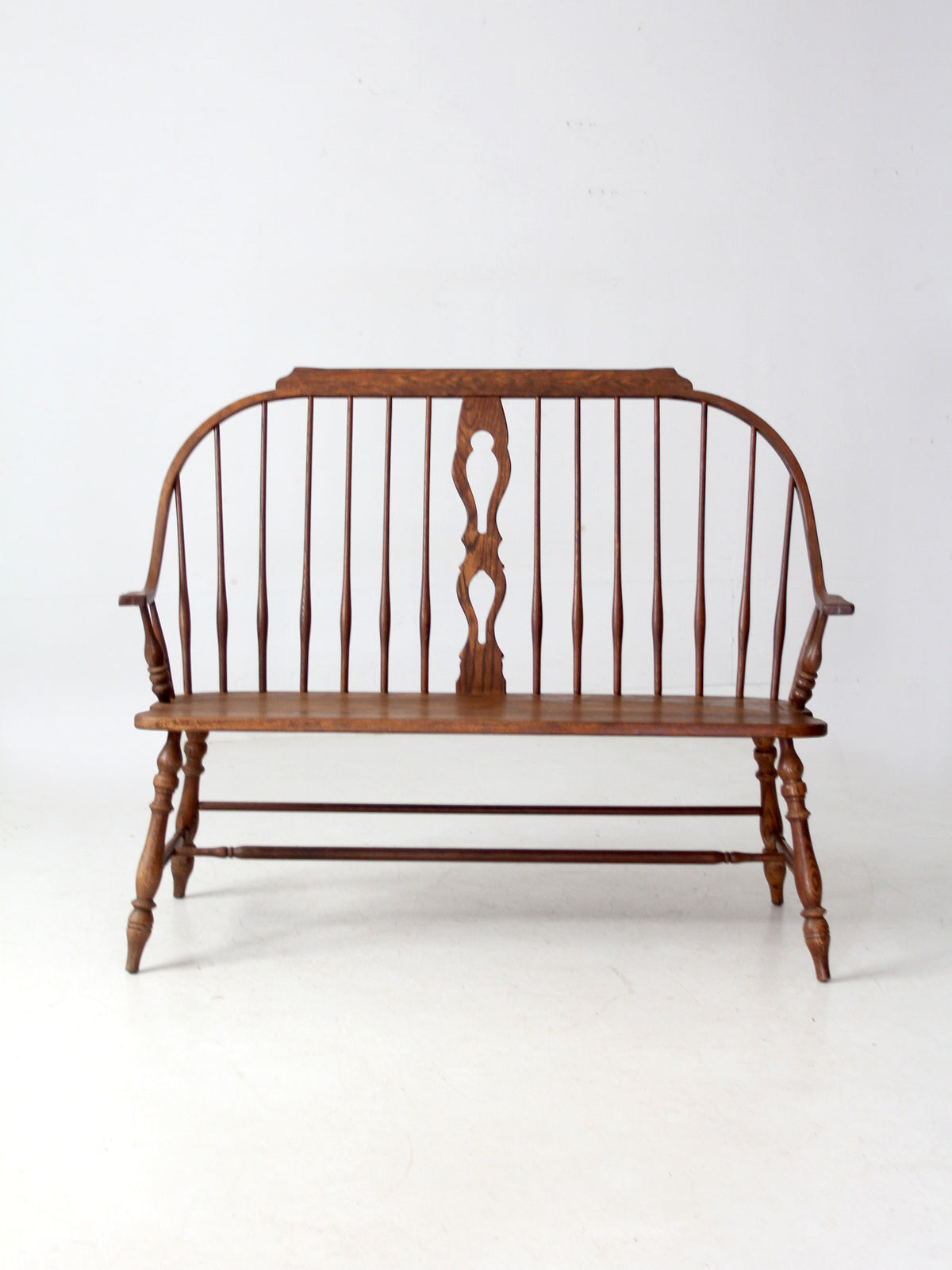 A traditional wooden spindleback bench with turned legs and a curved backrest, shown against a plain white studio background.