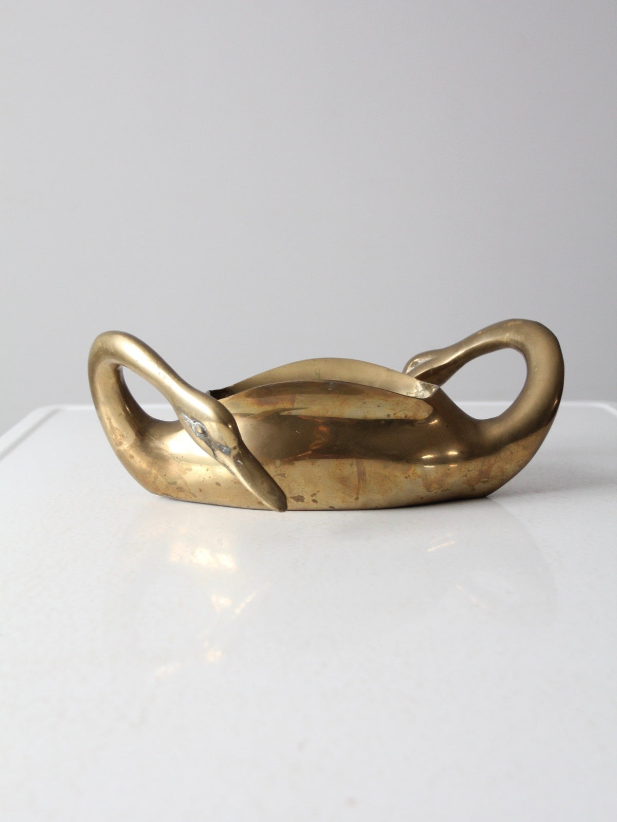 A  sculptural brass swan planter with two looped handles and a smooth curved body, photographed on a white surface against a light gray background.