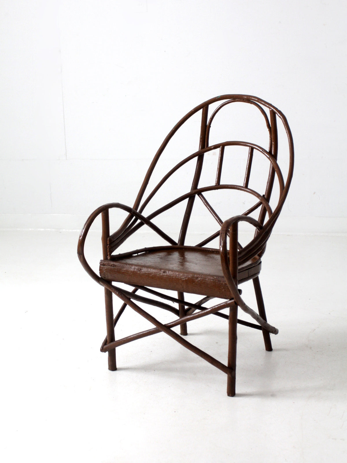 A dark brown antique Adriondack accent chair with a curved backrest, armrests, and a woven seat, photographed against a plain white studio background.