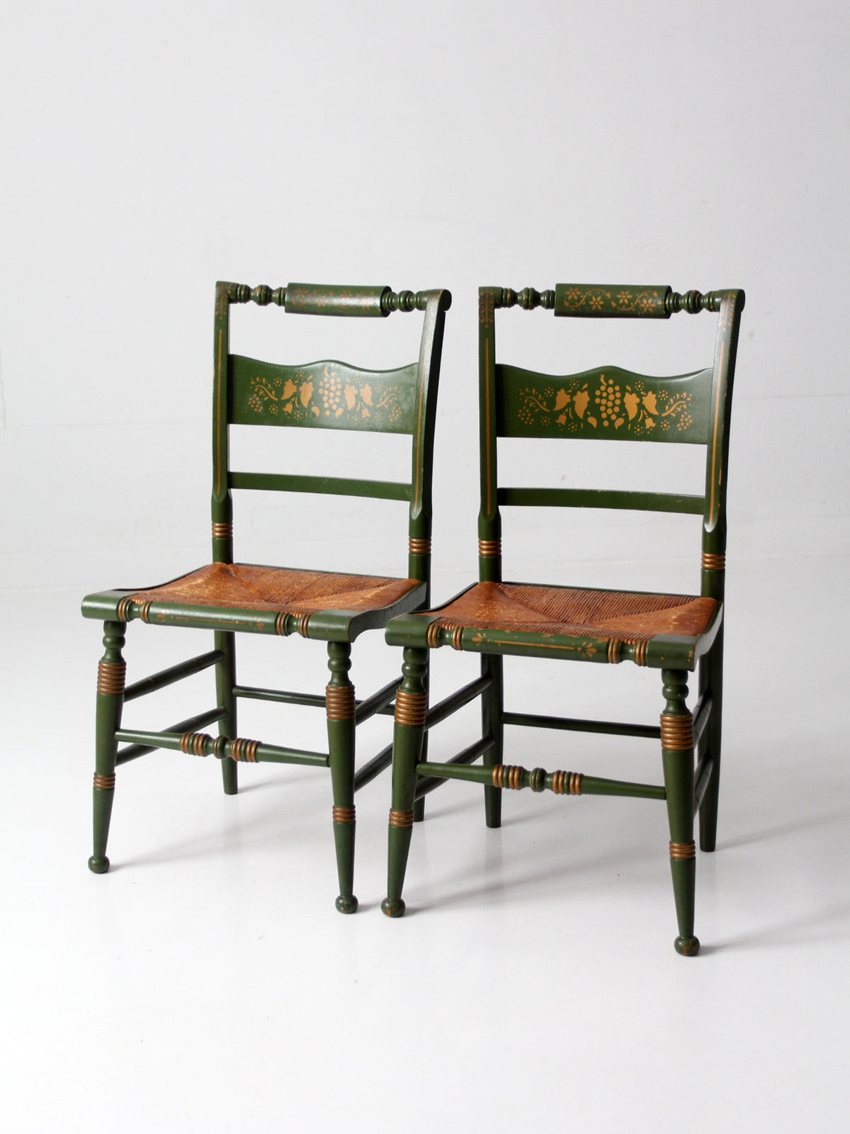 Two early 20th century Tell City green-painted chairs with brown rush seats on a white background