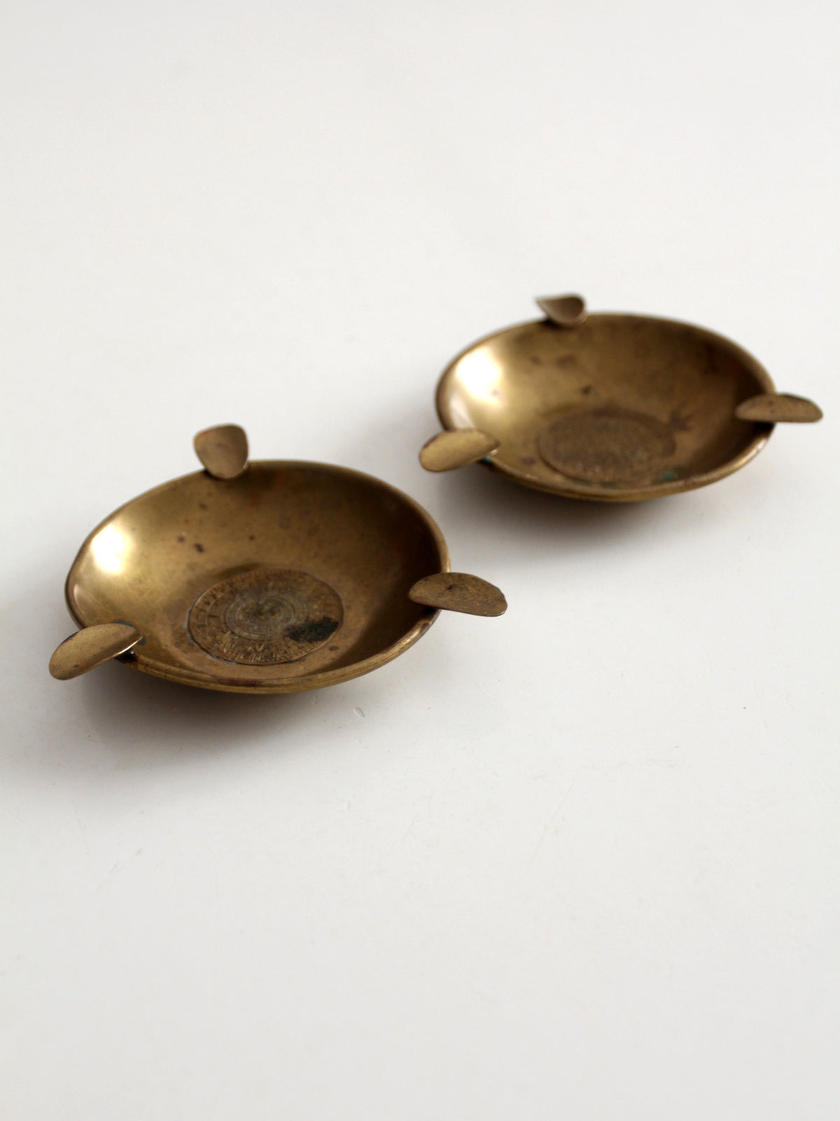 pair of vintage brass ashtrays with embossed medallions