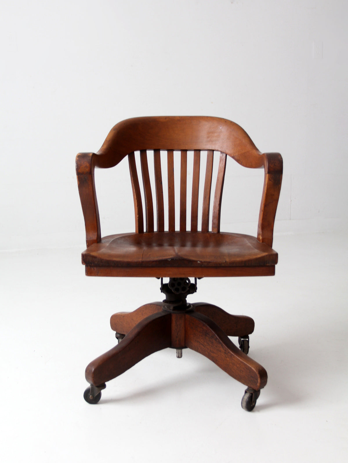 A classic wooden swivel office chair with a curved backrest, vertical slats, and a five-star caster base, shown against a plain white studio background.